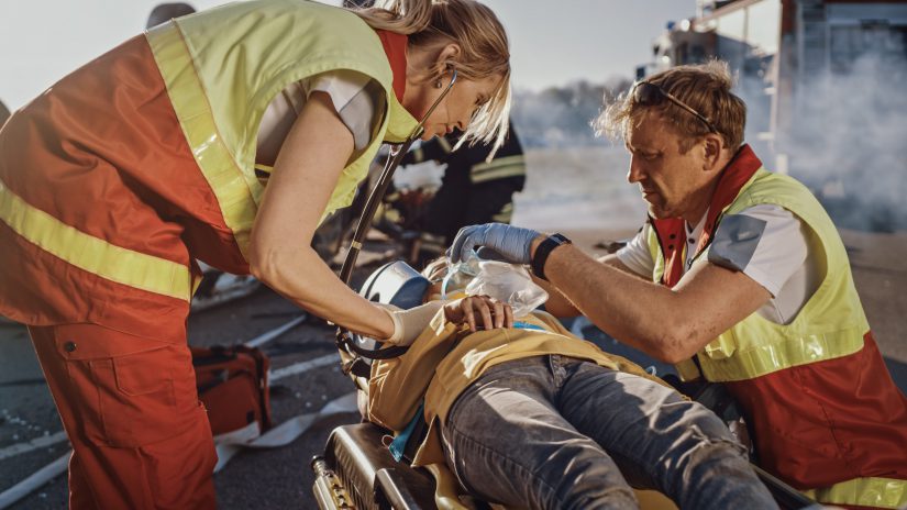 On the Car Crash Traffic Accident Scene: Paramedics Saving Life of a Traffic Accident Victim who is Lying on Stretchers. They Listen To a Heartbeat, Apply Oxygen Mask and Give First Aid Help